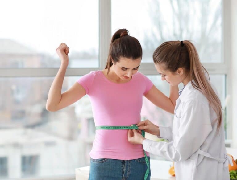 Aprenda como medir a cintura corretamente e acertar na circunferência 1 Profissional medindo a cintura de uma mulher
