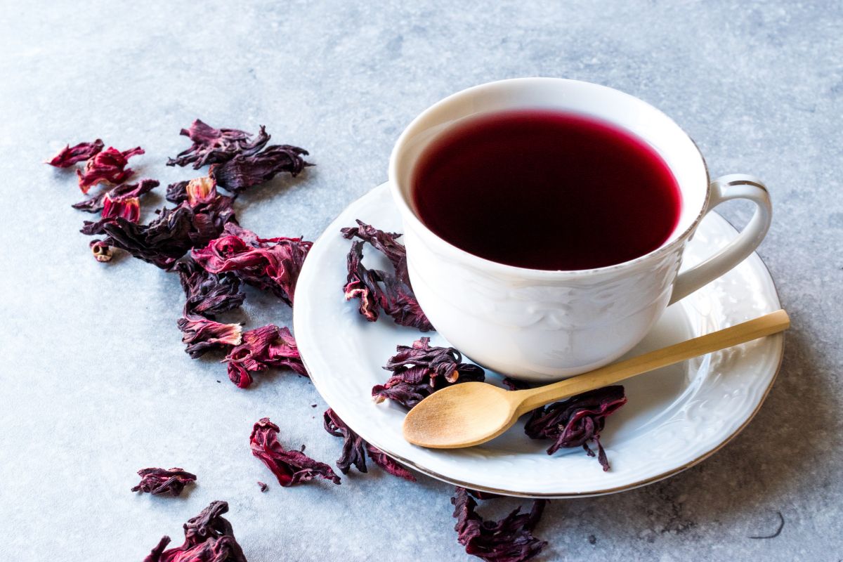 Chá de hibisco faz urinar muito? Entenda os efeitos diuréticos da bebida 1 Xícara contendo chá de hibisco com algumas pétalas secas de hibisco.